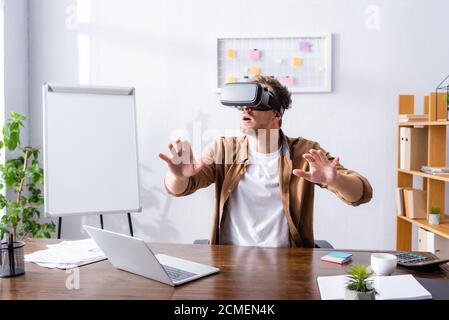 excited businessman gesturing while using vr headset at workplace Stock Photo