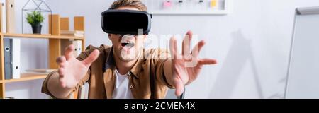 horizontal image of excited businessman gesturing while using vr headset in office Stock Photo