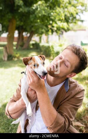 young man making duck face while holding jack russell terrier dog in park Stock Photo