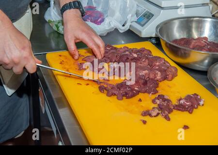 Men's hands slice chicken liver for cooking, on a cutting Board in the kitchen. The liver is cut to make a warm salad Stock Photo