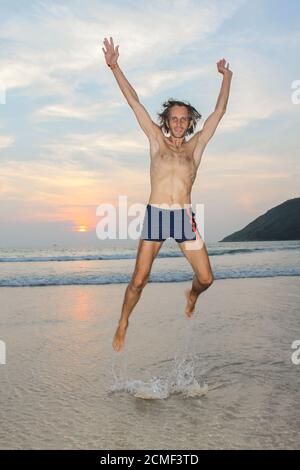 Man jumping happy on the beach with a sunset in the background Stock Photo