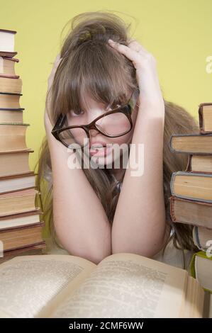 Girl sitting with lots of books and grabs his head. Stock Photo