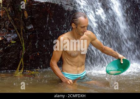 prospector panning gold in a river with sluice box   waterfall in the background Stock Photo