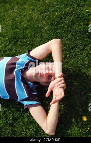Portrait of a young happy man relaxing on the grass with his hands under the head Stock Photo