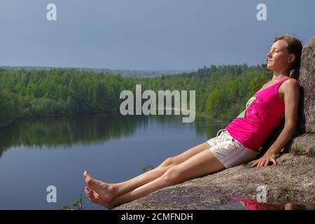 woman laying on cliff an relaxing above the lake Yastrebinoye, Priozersky district in Leningrad regi Stock Photo