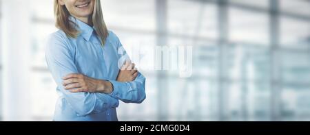 young smiling businesswoman wearing blue blouse standing with arms crossed in modern office. banner copy space Stock Photo