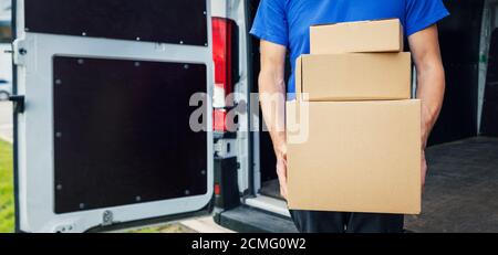 delivery person holding stack of boxes in front on van background. copy space Stock Photo