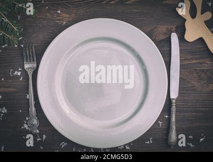 White plate with silver knife and fork on brown wooden surface Christmas table setting Stock Photo