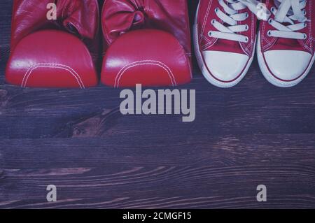 Red boxing gloves and a pair of red sneakers on a brown wooden surface Stock Photo