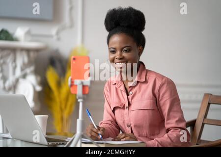 Focused African American millennial woman with afro hairstyle remote studying, working online on laptop, chatting with friends via video call on smart Stock Photo