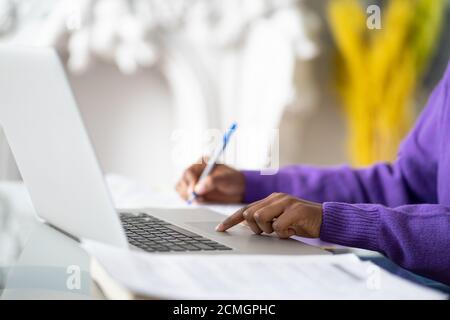 Close up of Afro-American woman employee or student using laptop, touches the touchpad with your finger, makes notes with pen. Selective soft focus. Stock Photo