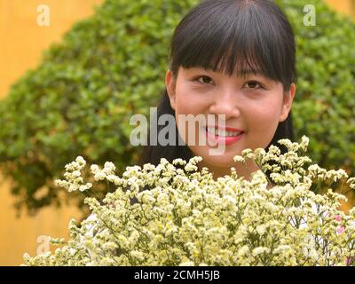 Beautiful young Vietnamese female florist shows a floral bouquet of statice cream flowers and smiles for the camera. Stock Photo