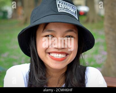 Cheerful Vietnamese girl from Hanoi wears a funny Parental Advisory Explicit Content bucket hat and smiles for the camera. Stock Photo