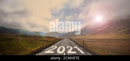 The word 2021 written on highway road in the middle of empty asphalt road at golden sunset and beautiful blue sky. Stock Photo