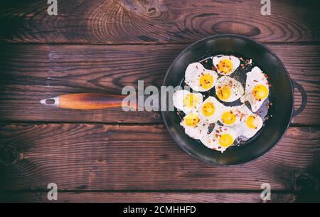 Fried quail eggs in a cast-iron black frying pan Stock Photo