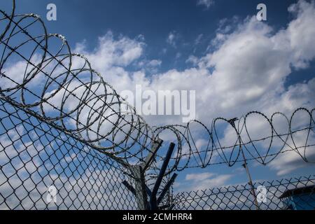 Barbed wire on top of metal mesh netting fence enclosing airport against cloudy sky