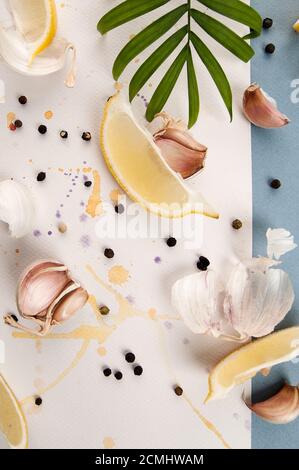 Garlic cloves, black pepper and lemon slices are on a white background with watercolor sprays. Stock Photo