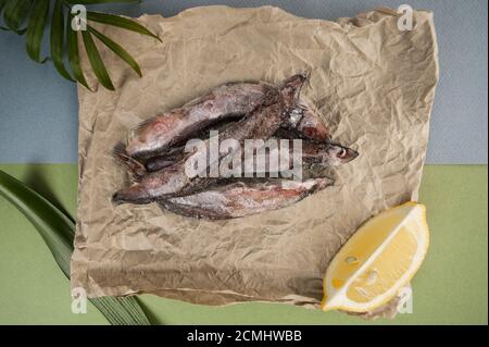 The raw frozen capelin rests on the kraft paper on a light blue-green background. Stock Photo