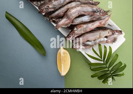 Raw fresh-frozen capelin, served with lemon on a light blue-green background. Stock Photo