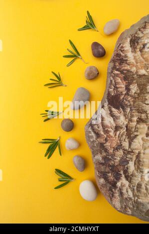 Minimalistic composition of multi-colored sea stones and leaves of fresh rosemary on a bright yellow Stock Photo
