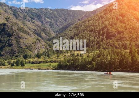 Tourist entertainment in Altai - rafting down the river on an inflatable boat against the background of mountains covered with green grass and trees a Stock Photo