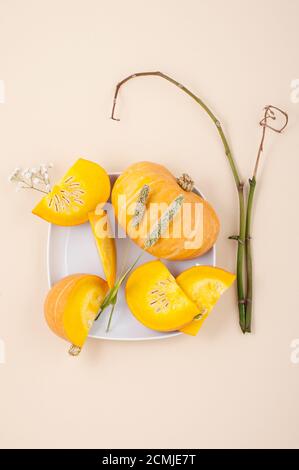 Fresh orange cut pumpkin and dried herbs on a light beige pastel background close-up. Stock Photo