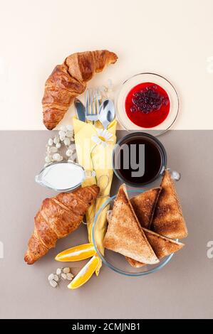 Black coffee, milk, croissants, jam, fruits and toast on a light yellow-brown combination background Stock Photo