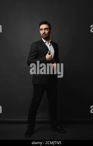 Full-length portrait of a handsome bearded gentleman in a black suit on the dark background. Stock Photo
