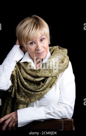 Portrait of an elderly woman adjusting her hair in a white shirt with a shawl on her shoulders again Stock Photo