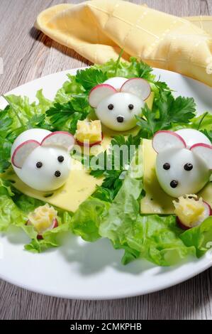 Serving a festive children's snack, boiled eggs in the form of mice in lettuce leaves and cheese cub Stock Photo