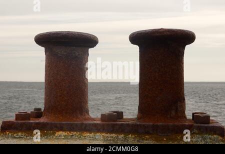 Rusty bollards for fixing the ropes of ships on a harbour wall with a view over the sea Stock Photo
