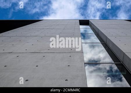 Modern building against blue cloudy sky. Bottom up view. Glass reflection and concrete facade, Berlin Stock Photo