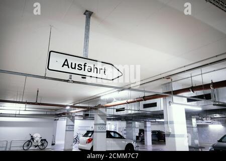 From the ceiling of an underground car park hangs a directional sign with the inscription in german 'Ausfahrt' - Exit. Stock Photo
