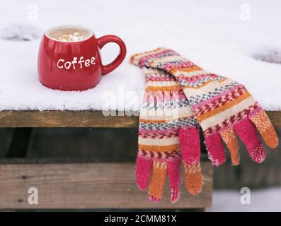 multi-colored knitted mittens and a red cup with coffee Stock Photo