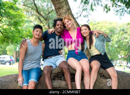 Friends sitting together on a trunk of a tree outdoors. Stock Photo