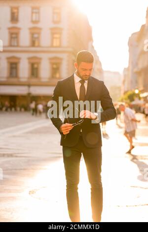 A handsome young businessman walking on the streets and checking the time on his wristwatch. Stock Photo