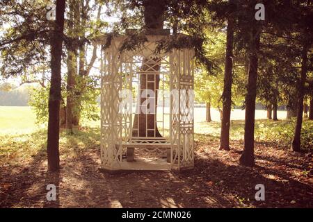 Small white gazebo and bench at the edge of the forest Stock Photo