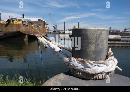 Mooring bollard with ship ropes. Bollard with mooring ropes on the quay. Moored ship at the port quay. Stock Photo