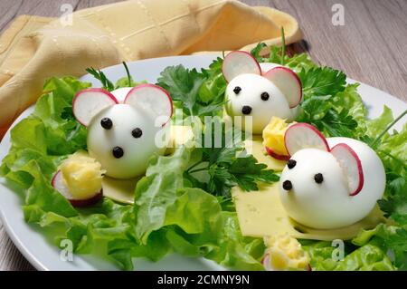 Serving a festive children's snack, boiled eggs in the form of mice in lettuce leaves and cheese cub Stock Photo