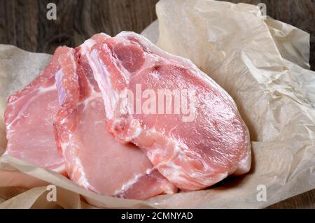 A pile of fresh chopped raw pork steaks over the bones in the wrapping paper on the table. Close-up. Stock Photo