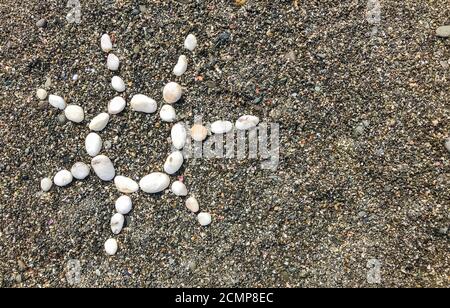Sun of white pebbles on dark sand by the sea copy space. Stock Photo