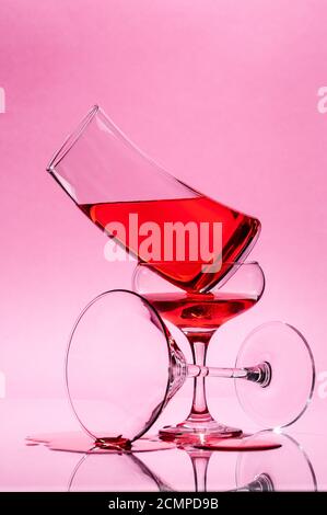 The composition of three glasses of different shapes with a red liquid on a light pink background. Stock Photo