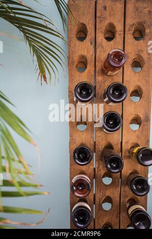 wine bottles in retro wooden rack with green house plant and blue wall, modern wine rack Stock Photo