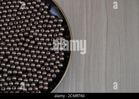 Plate, plate in black color with beads or round silver jewelry, on wooden background with copy space, photo zoom Stock Photo