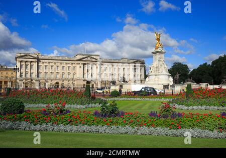 Scenic View of Buckingham Palace taken from Green Park, with flower beds in full bloom against a scenic blue cloudy sky and Queen Victoria Monument.