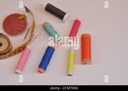 Spool of needles and threads of various colors, with tape measure, top view, on white background Stock Photo