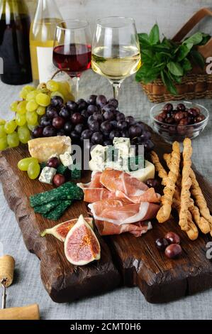 Dishes for a snack Antipasto on a wooden board with prosciutto, different kinds of cheese, grapes an Stock Photo