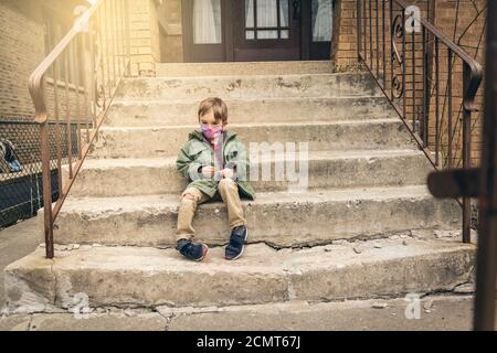 Boy sitting on the front steps with a face mask on during quarantine Stock Photo