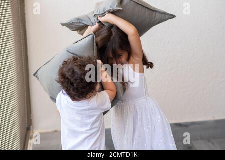 Happy children having pillow fight in home. A Brother and Sister having a playful pillow fight indoors in a neutral space. Soft focus to show movement. Stock Photo