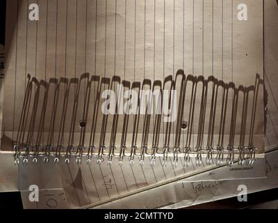 Long shadows from metal loops of ring bound notepad stretch across the lines of the ruled page in early evening low sunshine creating a strong pattern Stock Photo